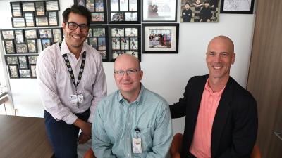 three men seated in an office, posed for camera