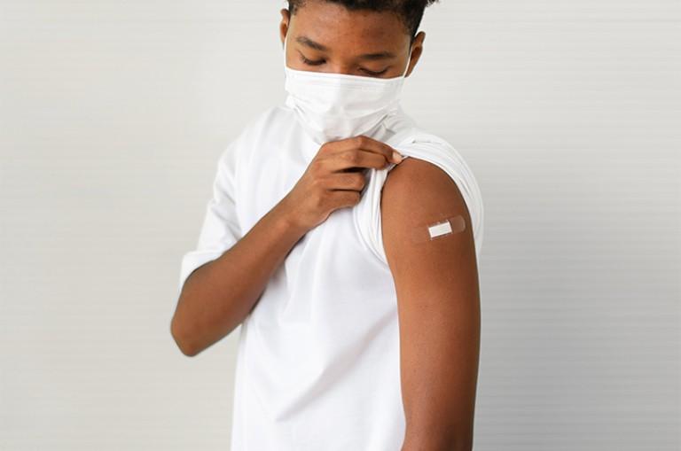 masked student pulling up his sleeve to show a band aid on his arm 
