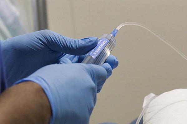 blue gloved hands holding a syringe with a tube coming from the end. 
