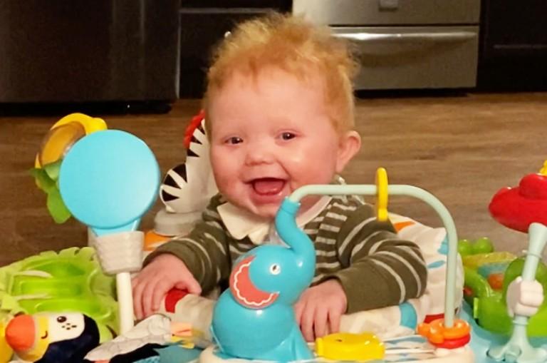 Smiling Baby in a baby walker with a tray full of toys