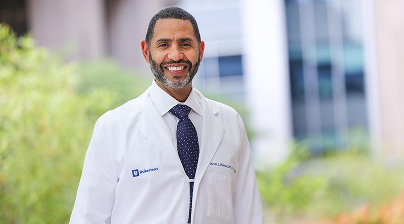 Black male physician in white coat standing outside