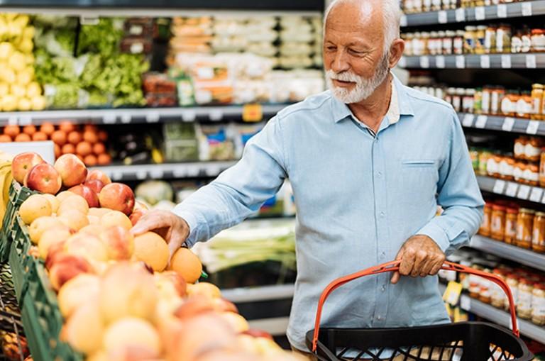 man with white beard and hair selecting produce at a grocery store