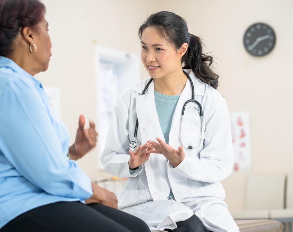 An Asian woman healthcare provider speaking with a Black woman patient.