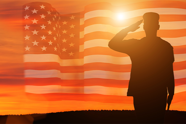 Silhouette of soldier saluting a flag waving in the sky at sunset
