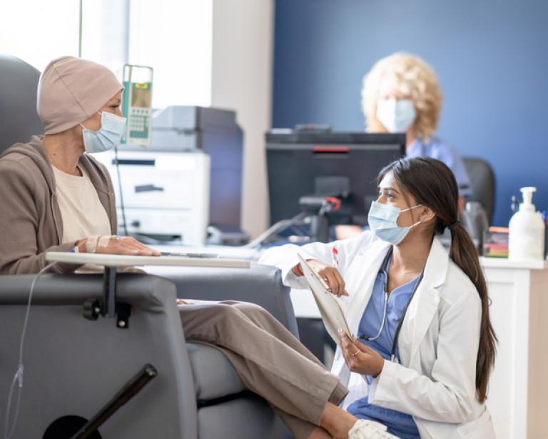 Provider kneeling in front of a cancer patient in an easy chair receiving cancer treatment.