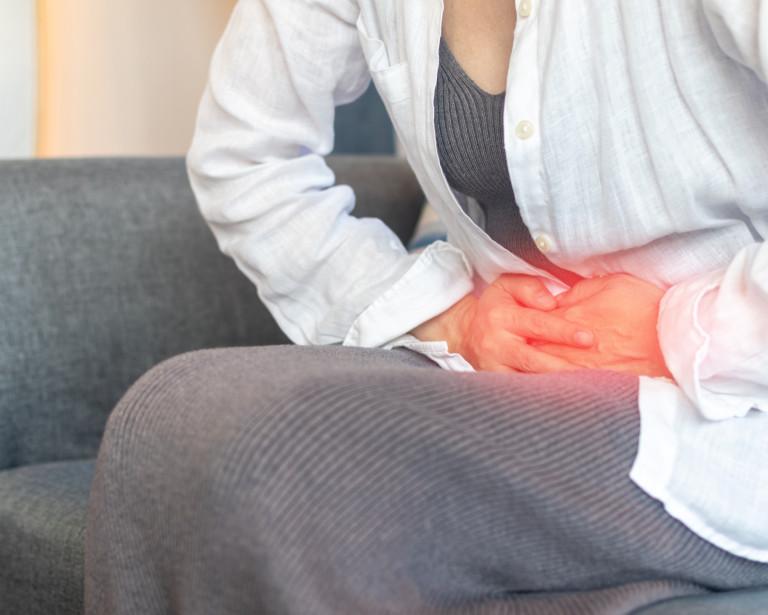 a woman's torso with her hands clutching her abdomen, highlighted in read to indicate severe pain.