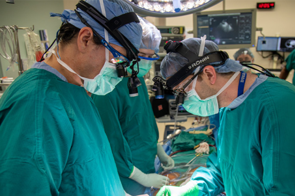 Three surgeons in the OR, masked and gowned, performing a heart transplant