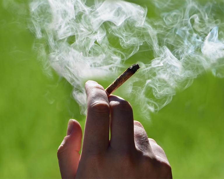 hand holding a cigarette, surrounded by smoke. 