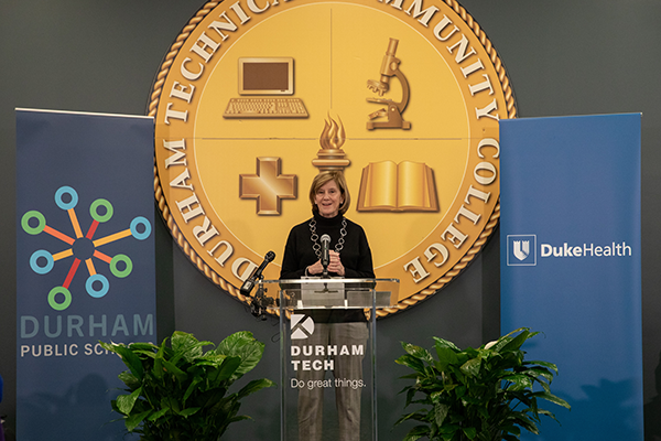 Mary Klotman, MD at a podium in front of the Durham Tech school seal.