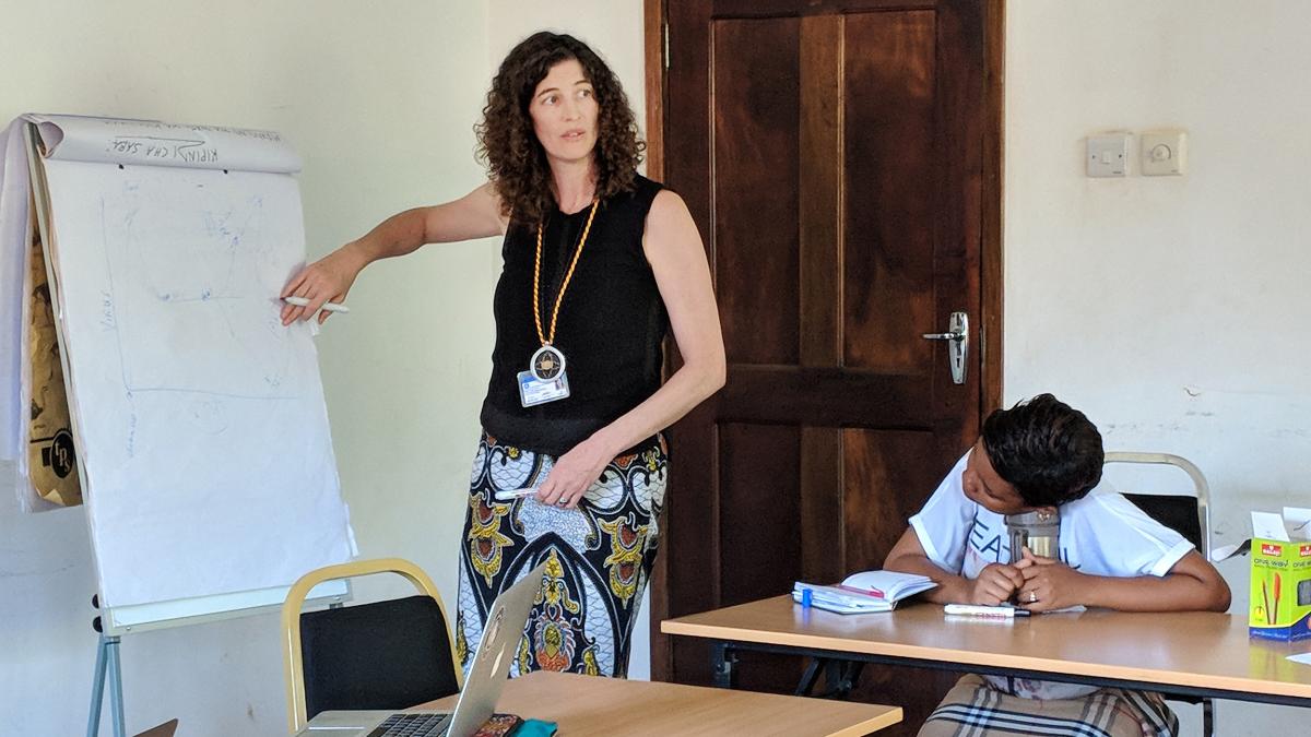 woman stands infront of classroom, student sitting at desk