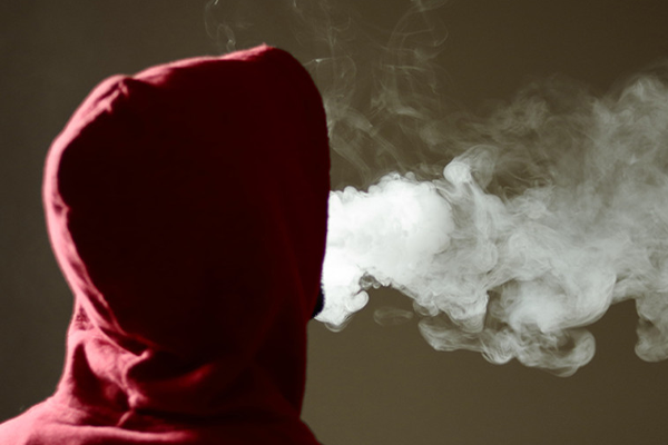 figure in a hoodie blowing smoke
