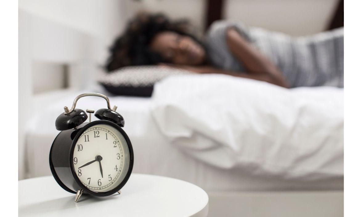 An alarm clock next to a sleeping person