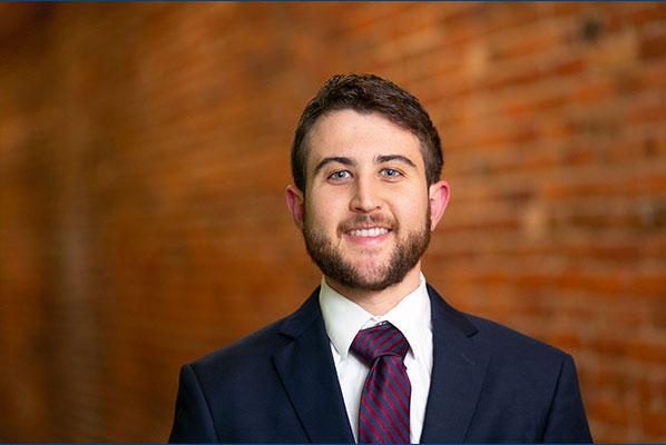 A young adult wearing a suite and tie smiles at the camera.
