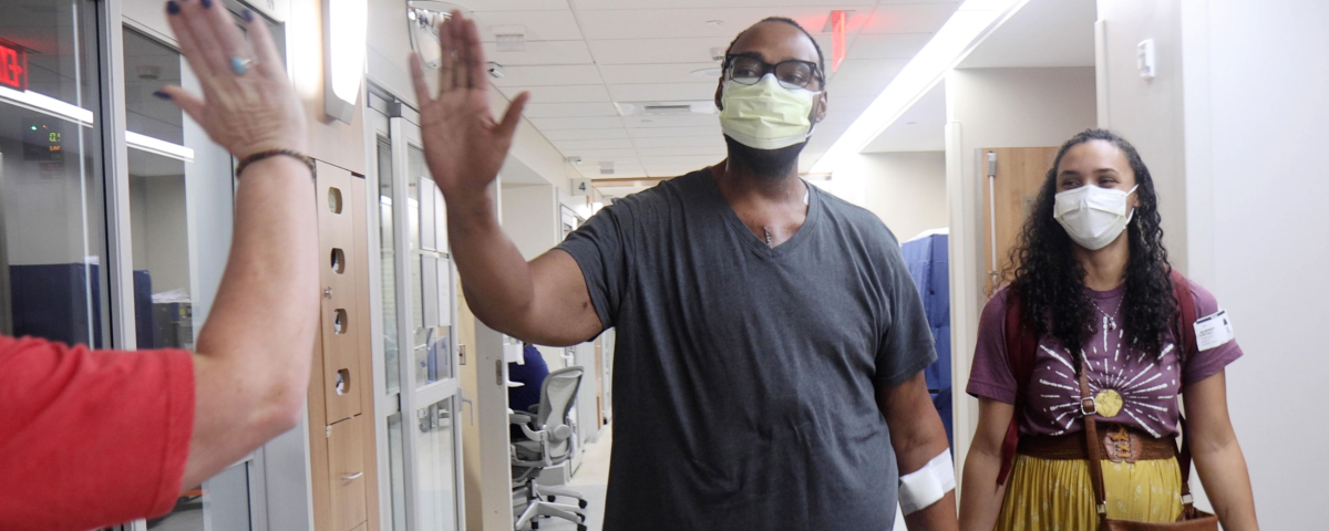 A man wearing a surgical masks high-fives a person off-camera while a woman looks on. 