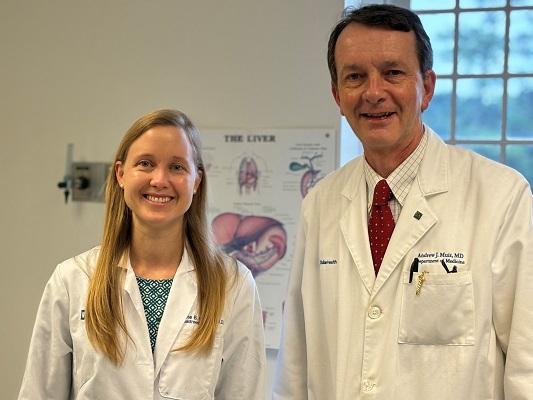 A young woman and an older man in medical coats, looking at the camera.