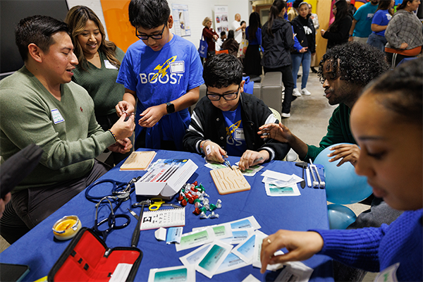 Duke med students Guissepe Yanez, MS3,  and Liban Mohamed, MS2, show BOOST students Gabriel Gil, 11, and Jonathan Sanchez, 11, how to suture during BOOST’s 20th anniversary celebration.