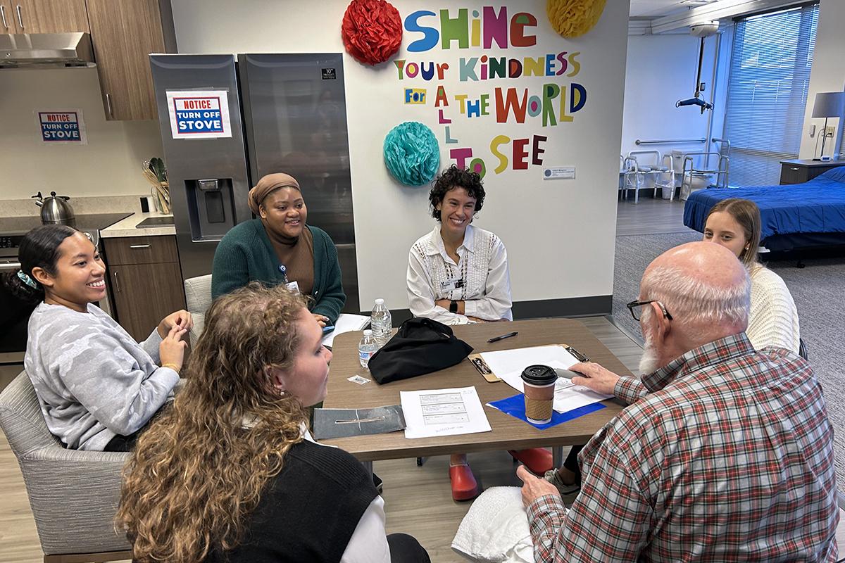 occupational therapy students and a client volunteer sitting at a table talking and smiling