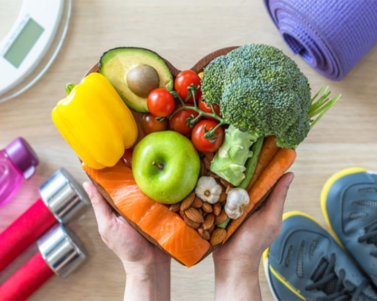 a heart shaped bowl of fruits, veggies, nuts, and salmon