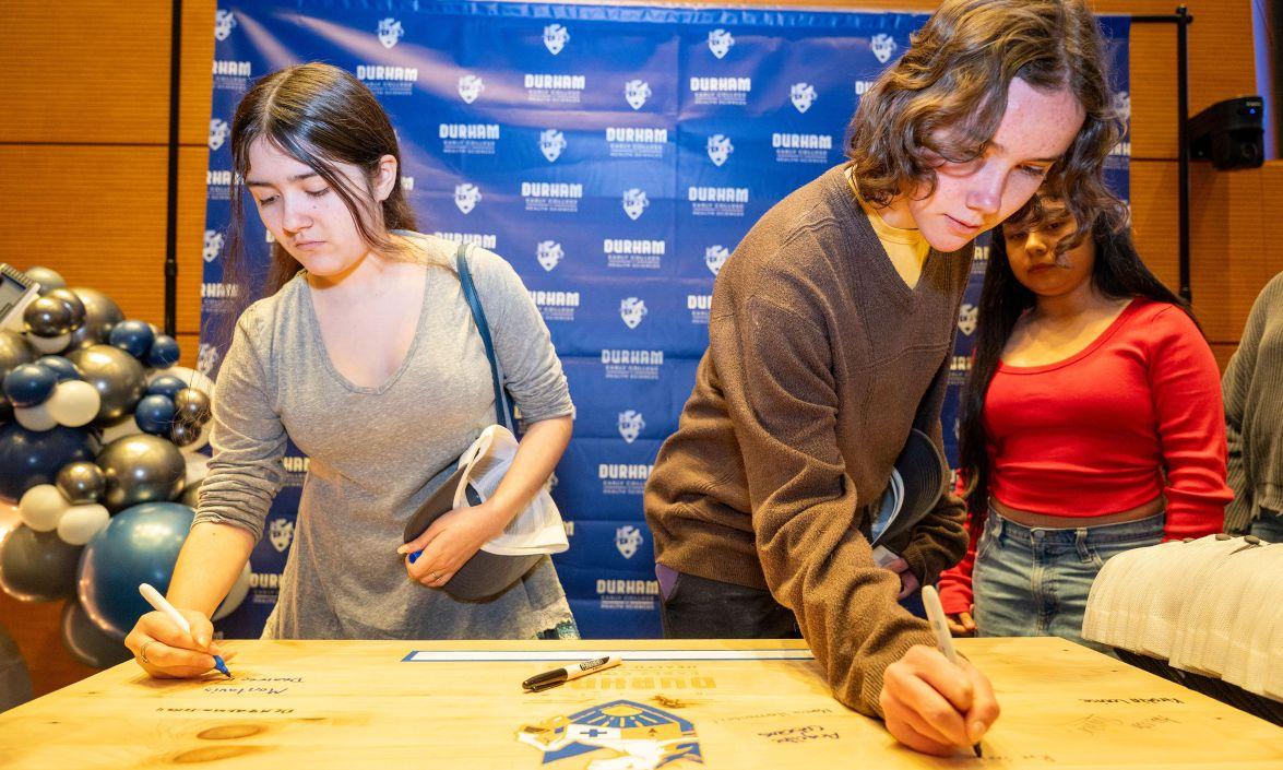 Students enrolling in the inaugural class of the new Early College of Health Sciences sign their names on a large placard.