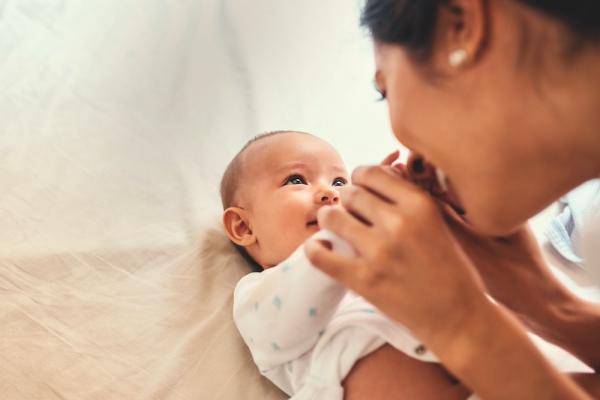 A smiling woman gently grasps hands with a baby who smiles back up at her