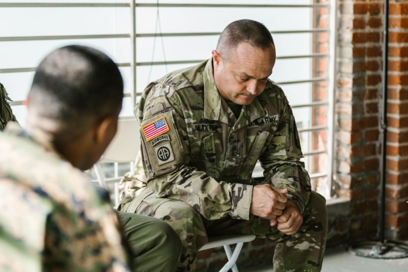 Two military personnel in uniform are seated and engaged in a discussion