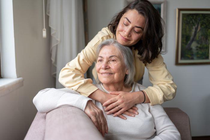 Older mother seated with daughter above with her arms around her mother