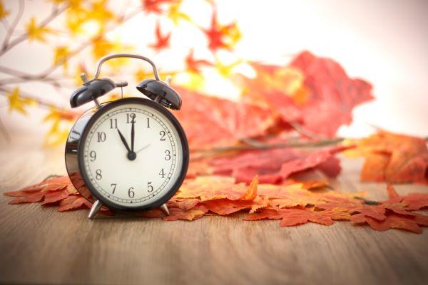 Alarm clock surrounded by orange autumn leaves