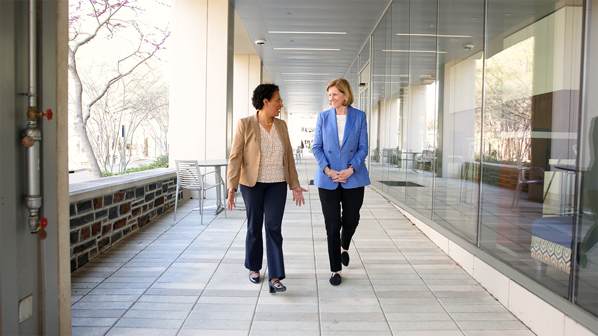 Dean Mary Klotman and Dr. Geeta Swammy walking together along a collinade. 