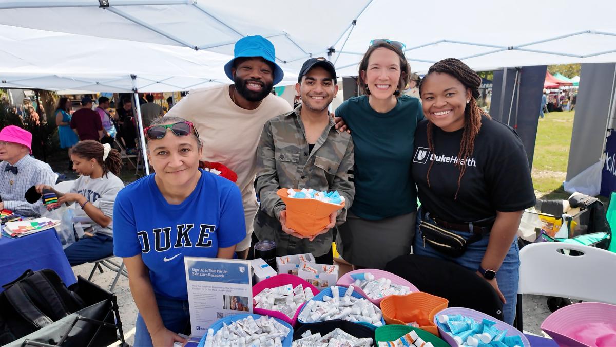 Smiling group of facutly, staff, and students from Duke Dermatology at Durham Pride booth