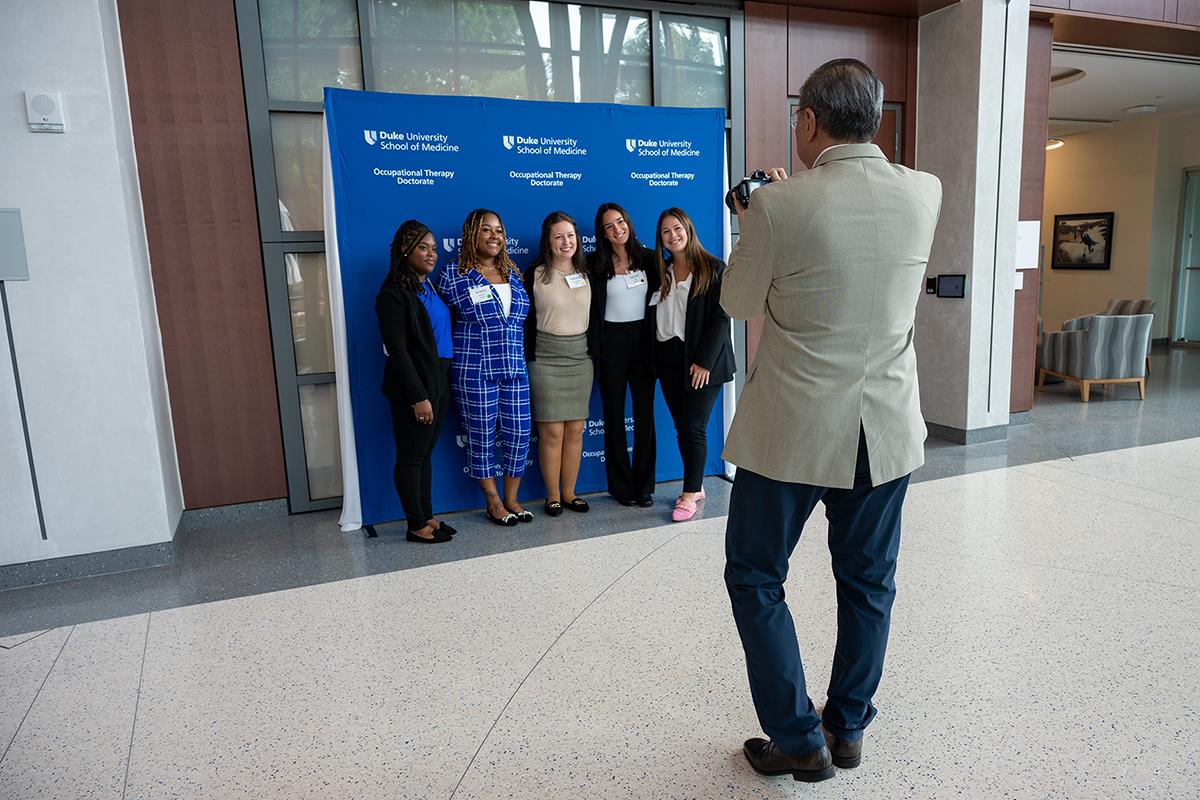 five students posing for a photo in the background with a photographer in the foreground