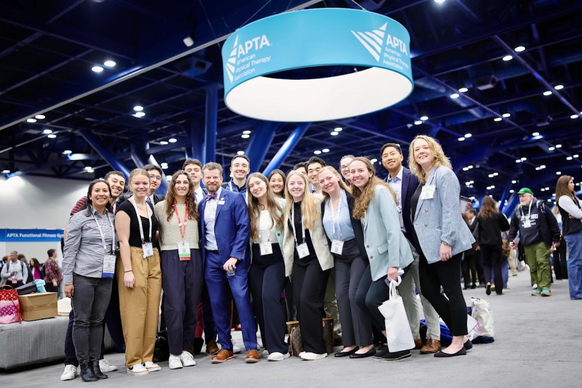 more than a dozen students and faculty posing for a group photo on the floor of the APTA CSM conference