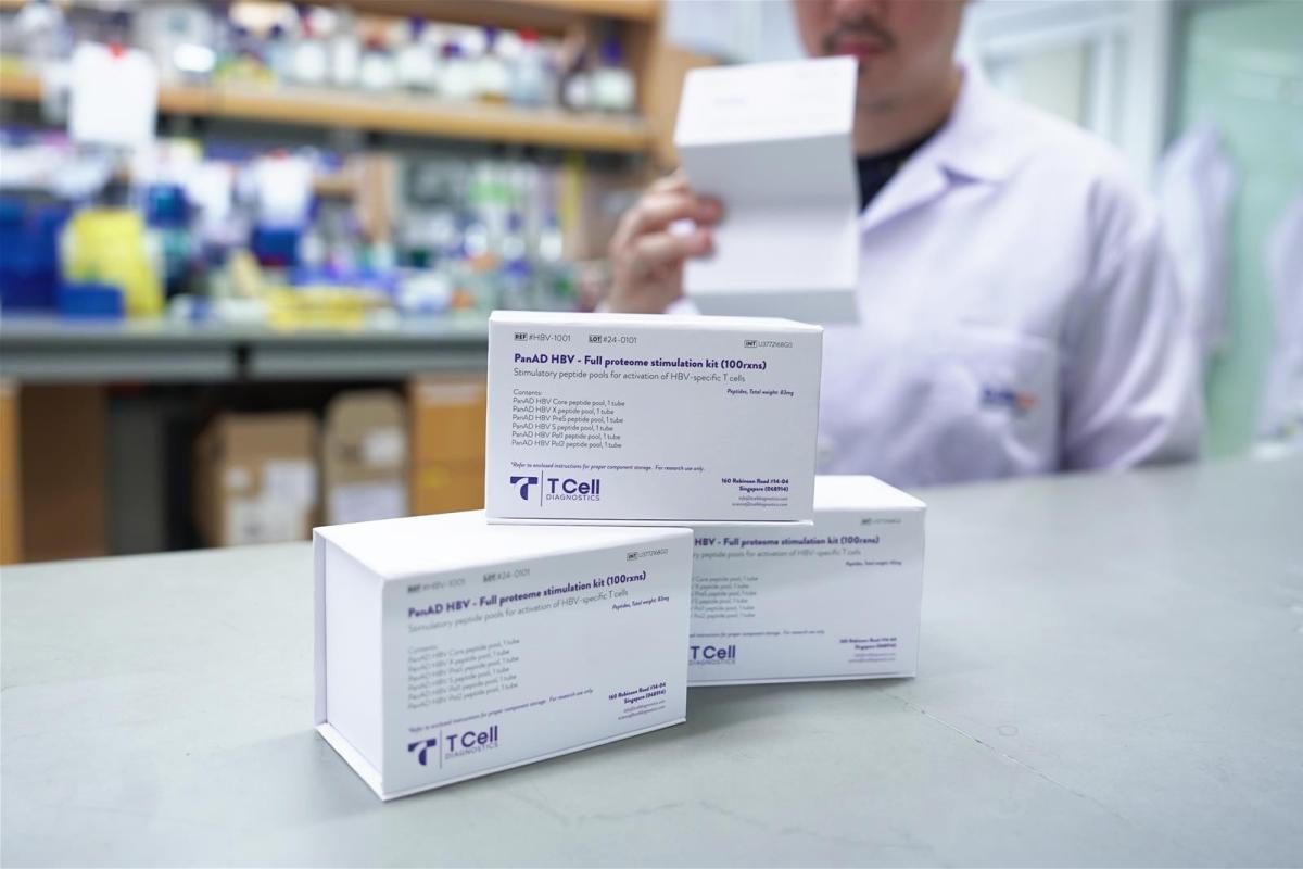 Image: A man in a lab coat stands with three boxes, suggesting involvement in a laboratory or research activity.