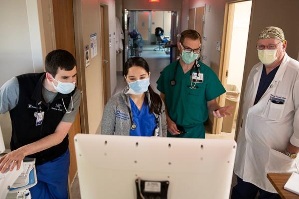 two medical students look at computer screen with two providers in hospital