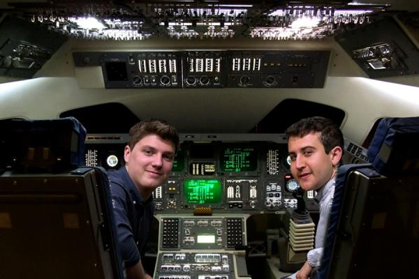 Two students sitting in the cockpit of a model of the space shuttle