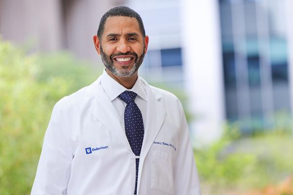 Black male physician in white coat standing outside