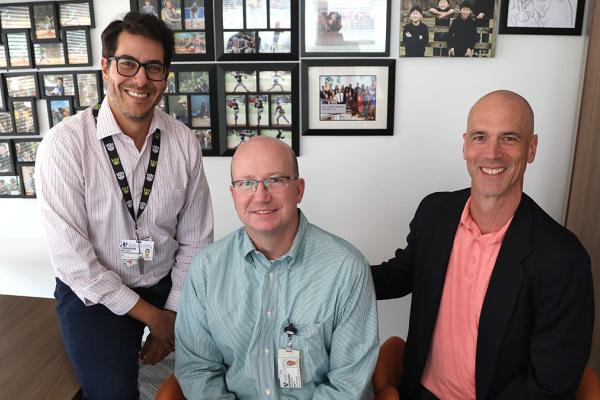 three men seated in an office, posed for camera