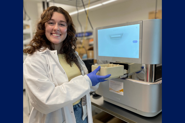 Woman working in the lab and standing next to a NextSeq 1000 sequencer