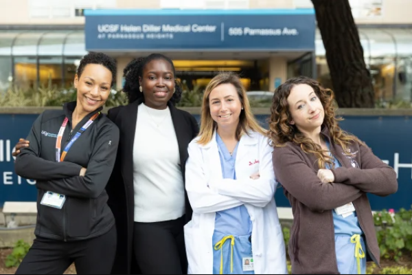 Four female doctors standing together with arms crossed, smiling in front of UCF front doors
