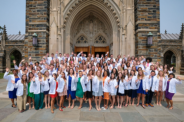 A group of students in white coats standing in front of the Duke Chapel