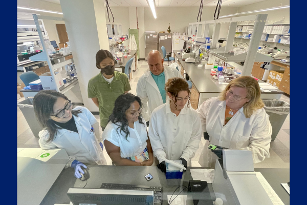 A group of scientists -- 4 in the front, 2 in the back -- gathered around a sequencer