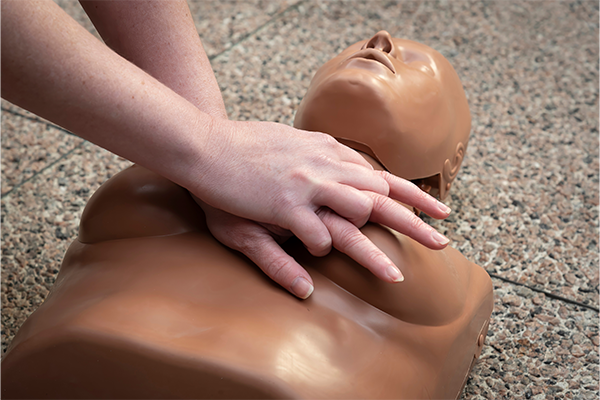two hands performing compressions on a mannequin with breasts