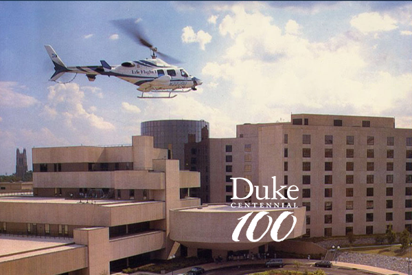 Life flight helicopter landing on the roof of Duke Hospital. Centennial logo in the foreground