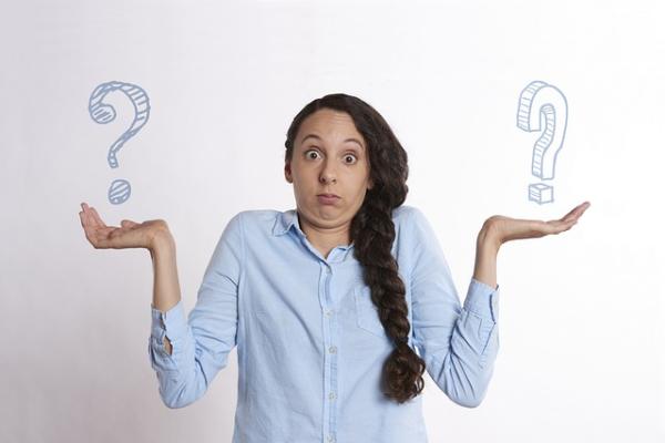 Photo of a woman holding up two question marks while shrugging her shoulders