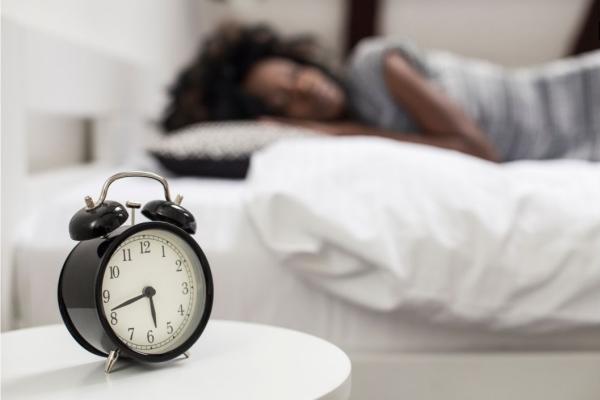 An alarm clock next to a sleeping person