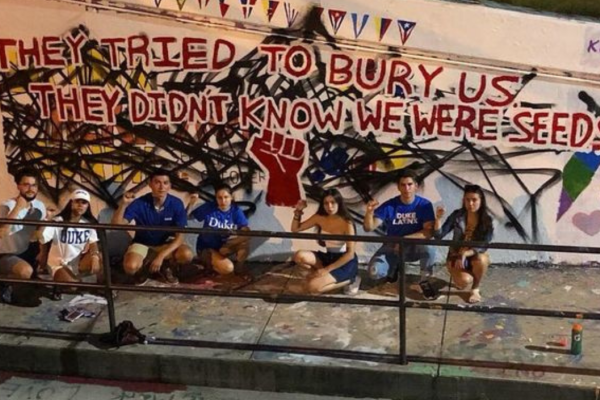 students with fists raised in front of mural
