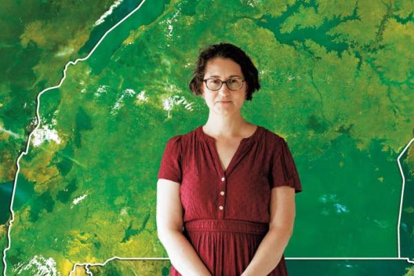 A woman in a burgundy dress stands in front of a green map.