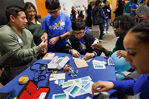 Duke med students Guissepe Yanez, MS3,  and Liban Mohamed, MS2, show BOOST students Gabriel Gil, 11, and Jonathan Sanchez, 11, how to suture during BOOST’s 20th anniversary celebration. 