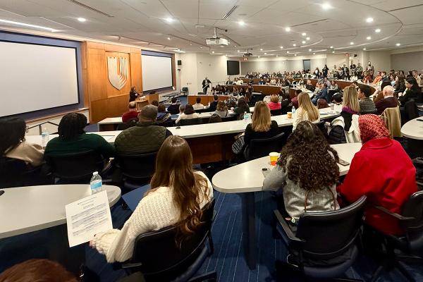 a lecture hall full of guests looking on as a staff member talks to them at the podium