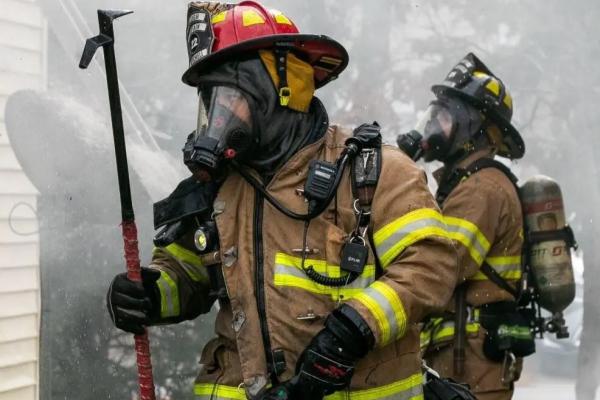 Two firefighters in heavy gear and gas masks fight a fire.