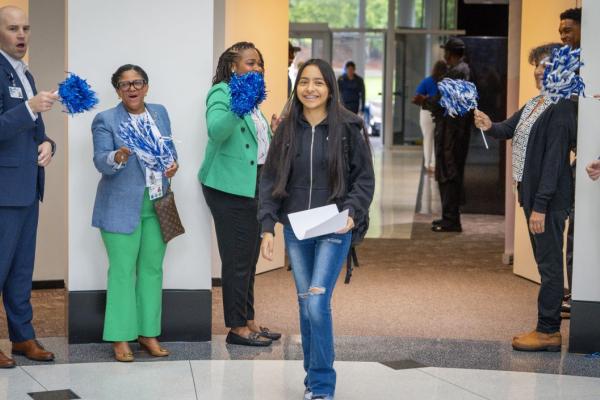 A rising 9th-grader enters the Durham Early College of Health Sciences while teachers and administrators cheer and wave pompoms.